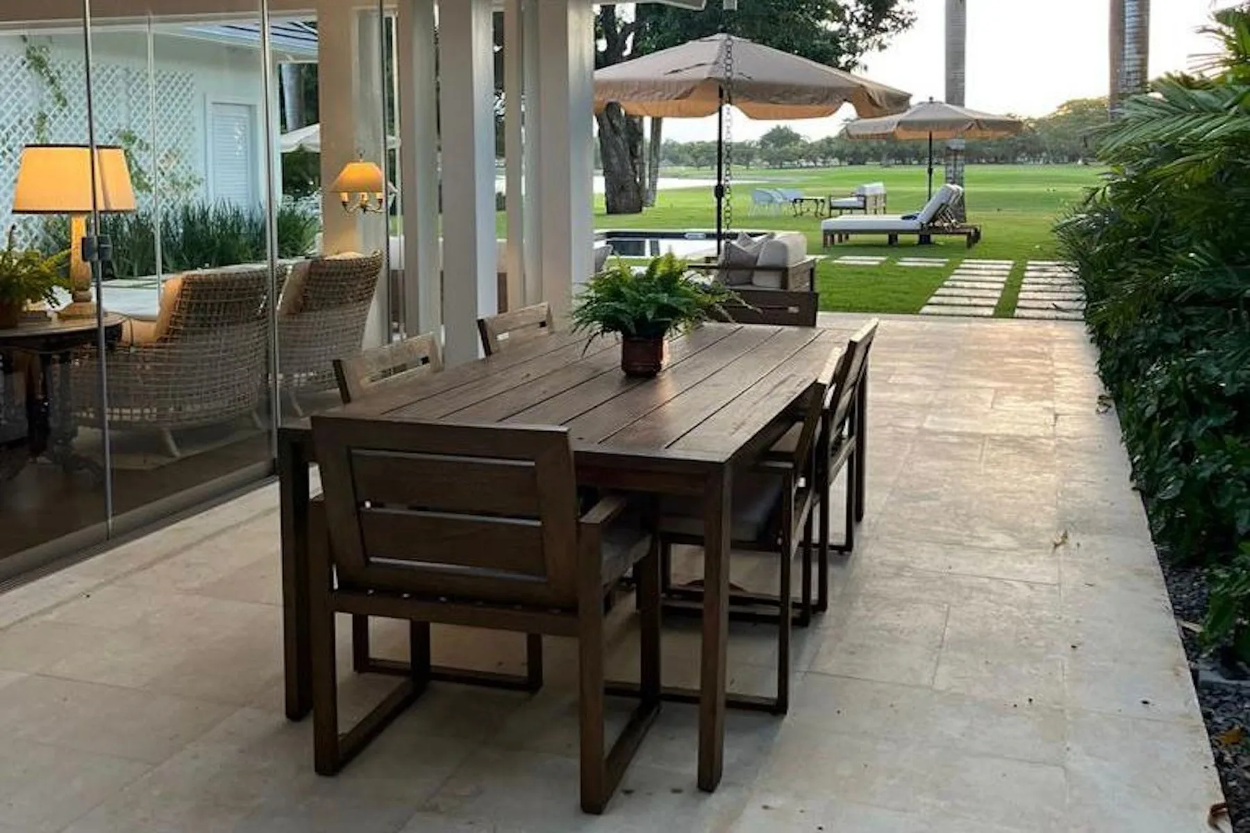 A covered outdoor dining area with a wooden table and garden beyond.