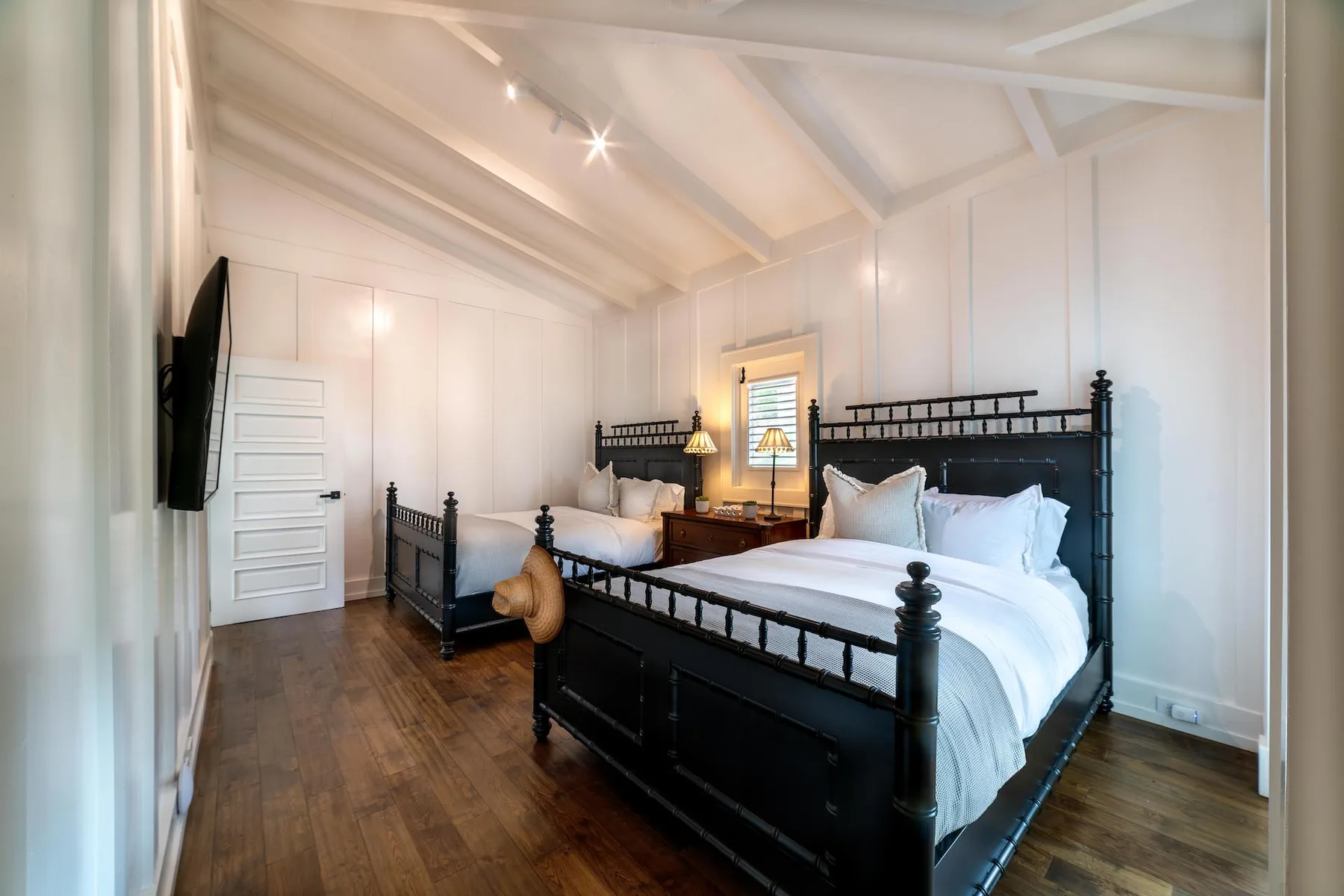 A bright bedroom with two beds, white bedding, and a sloped ceiling.