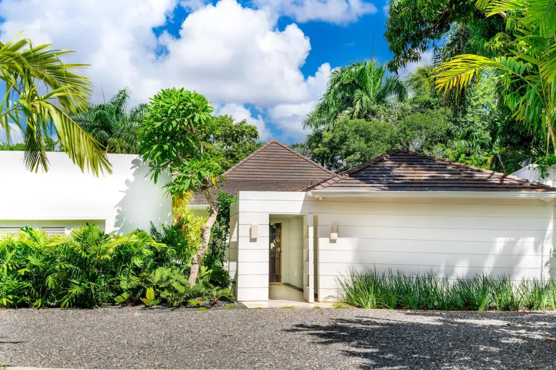 A low white building with a tiled roof stands among tropical greenery.