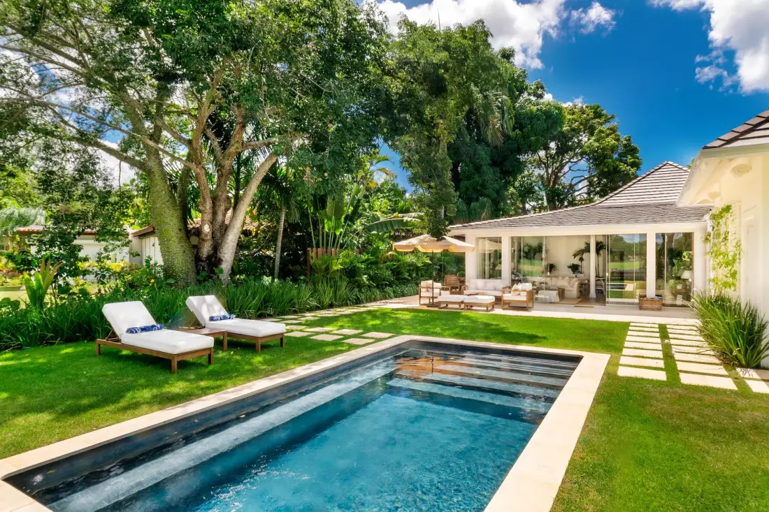 A garden patio with a swimming pool, lounge chairs, and a glass-enclosed seating area.