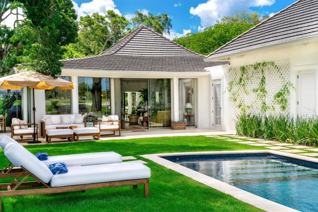 Un patio soleado con asientos al aire libre, césped verde y una piscina.