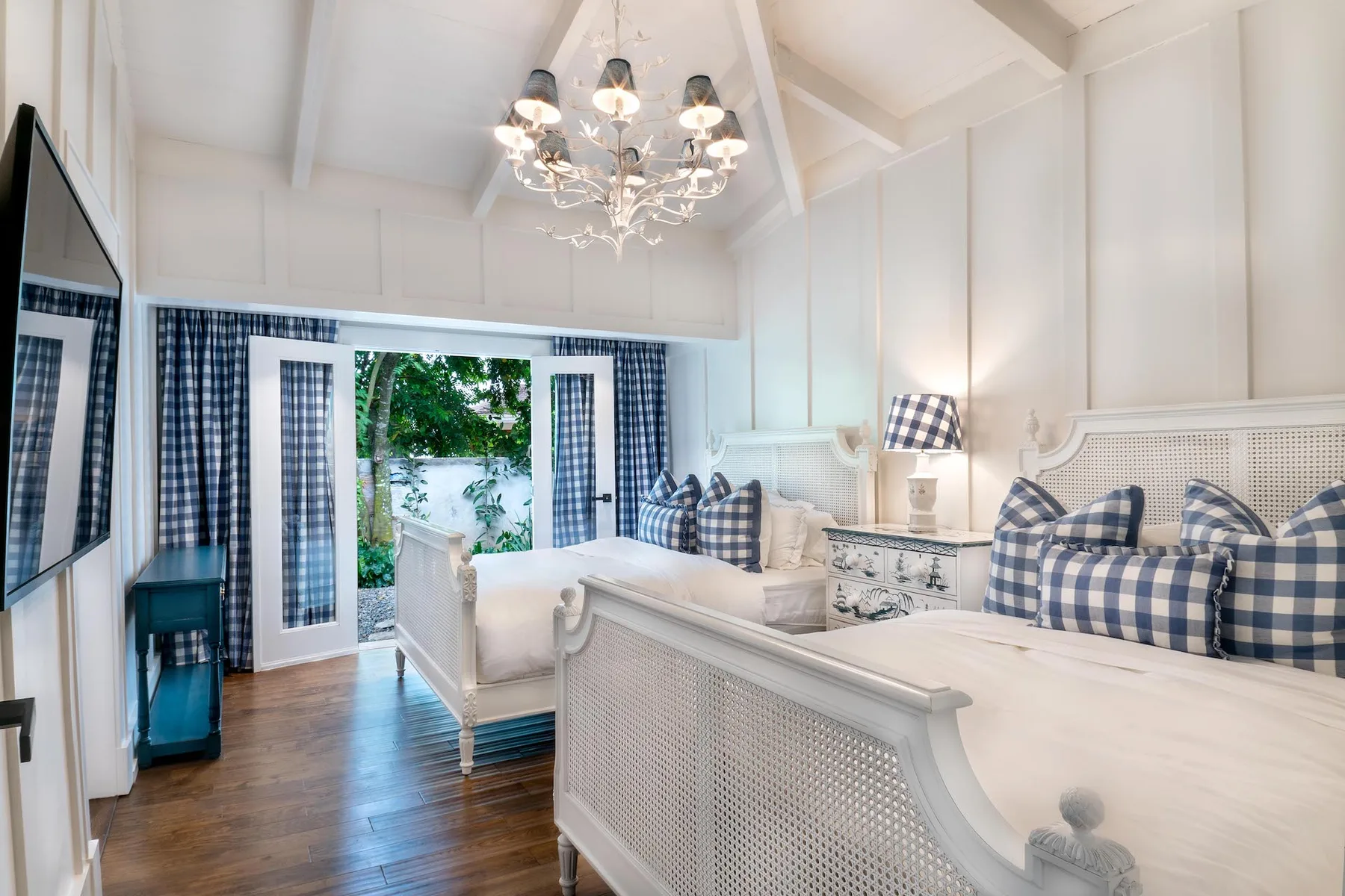 A bright bedroom with two beds, plaid bedding, and a chandelier.