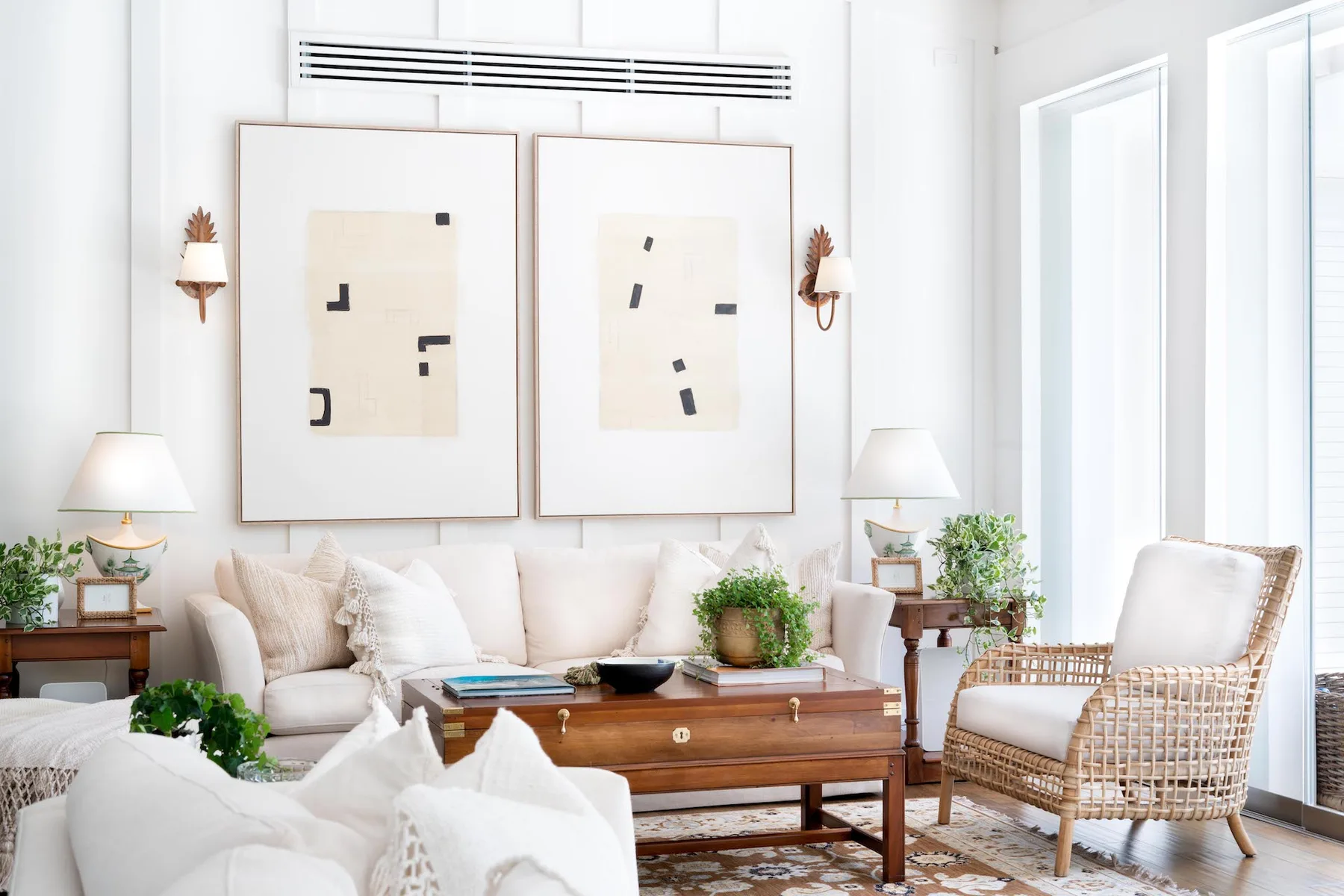 A bright living room with light-colored seating, framed abstract art, and a wooden coffee table.