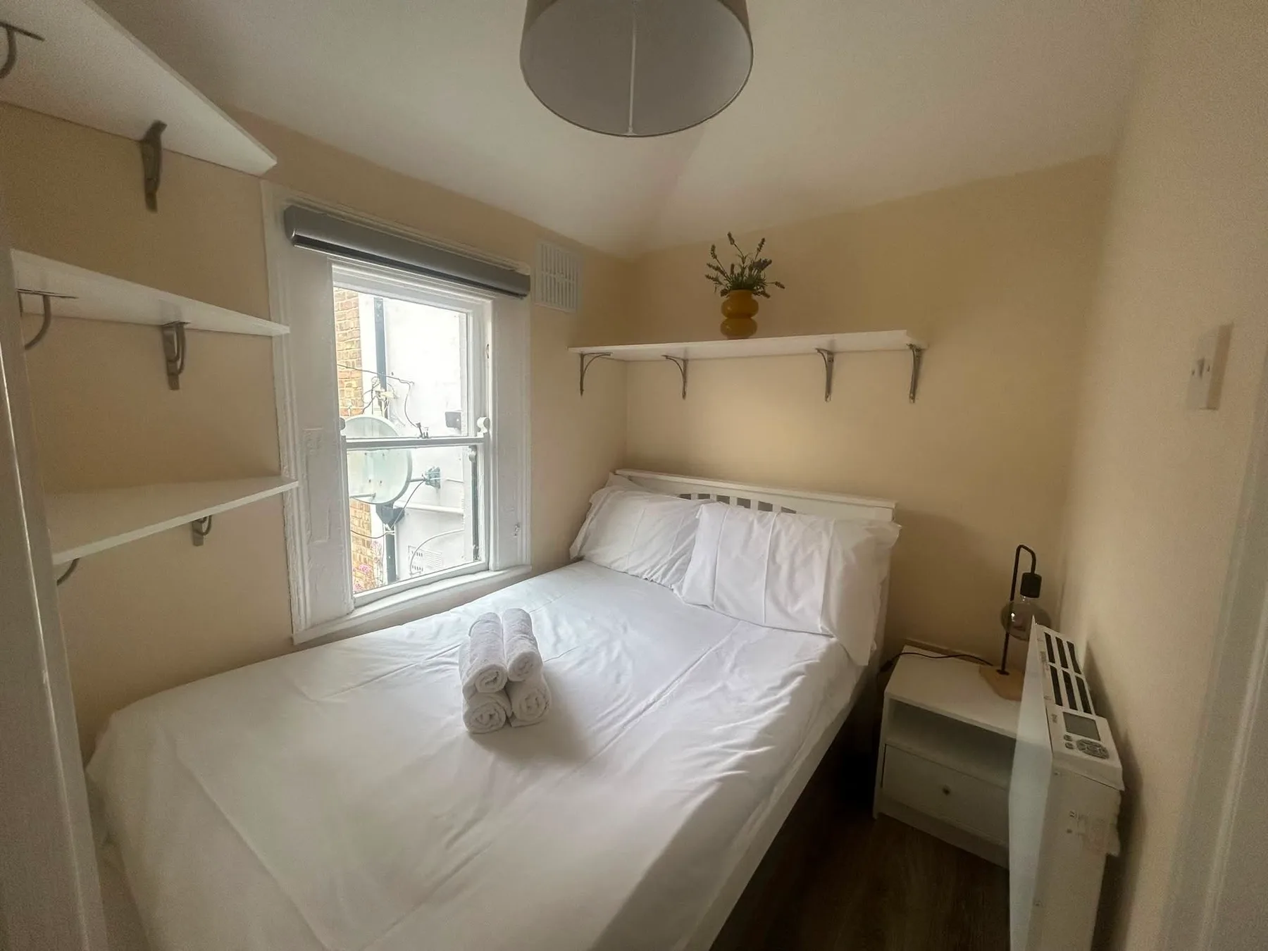 A bedroom with a white bed and shelves beside a window.
