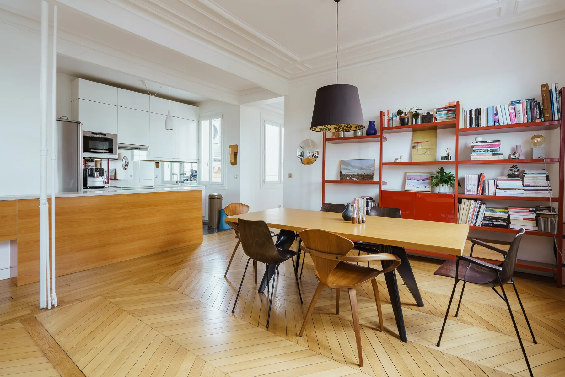 Un comedor luminoso con una mesa larga junto a estanterías abiertas y una cocina.