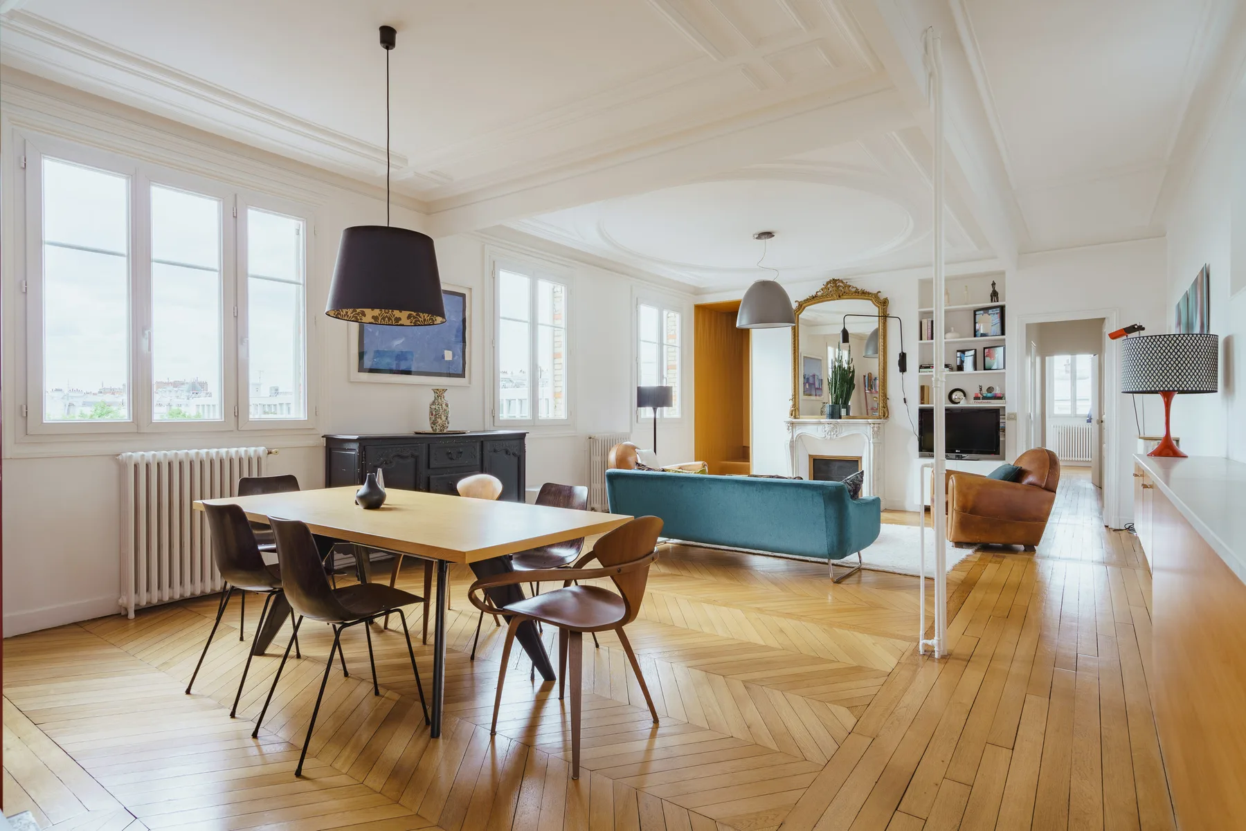 A bright open-plan living and dining room with a dining table and teal seating.