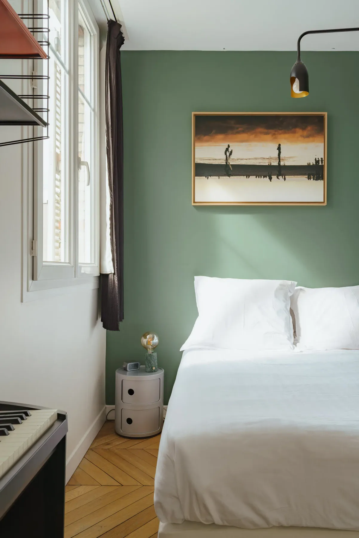 A bedroom with a white bed against a green wall.