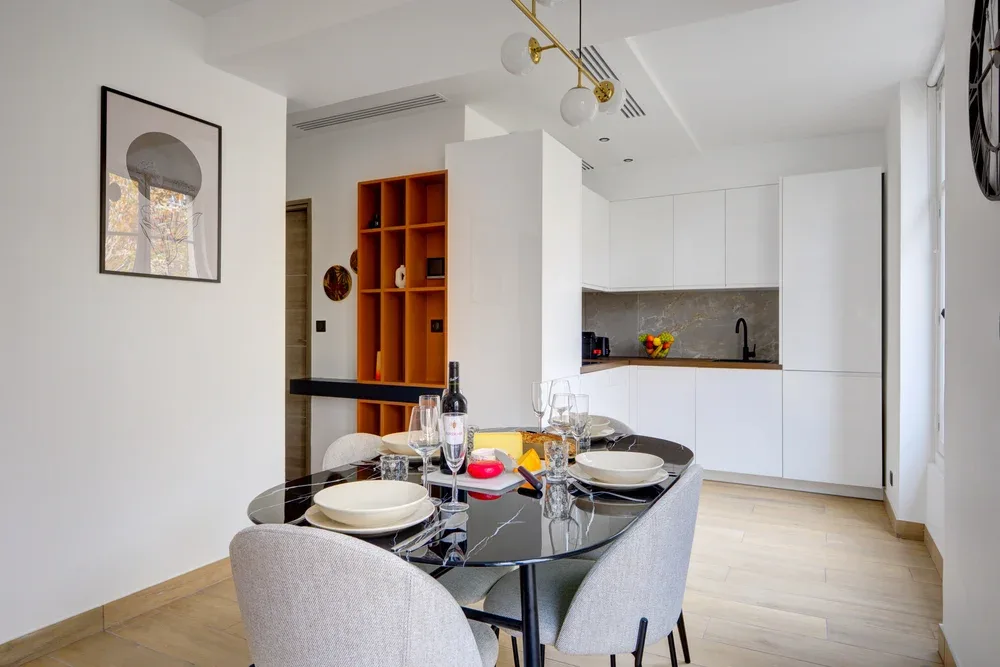 Un comedor con la mesa puesta junto a una cocina luminosa y moderna.