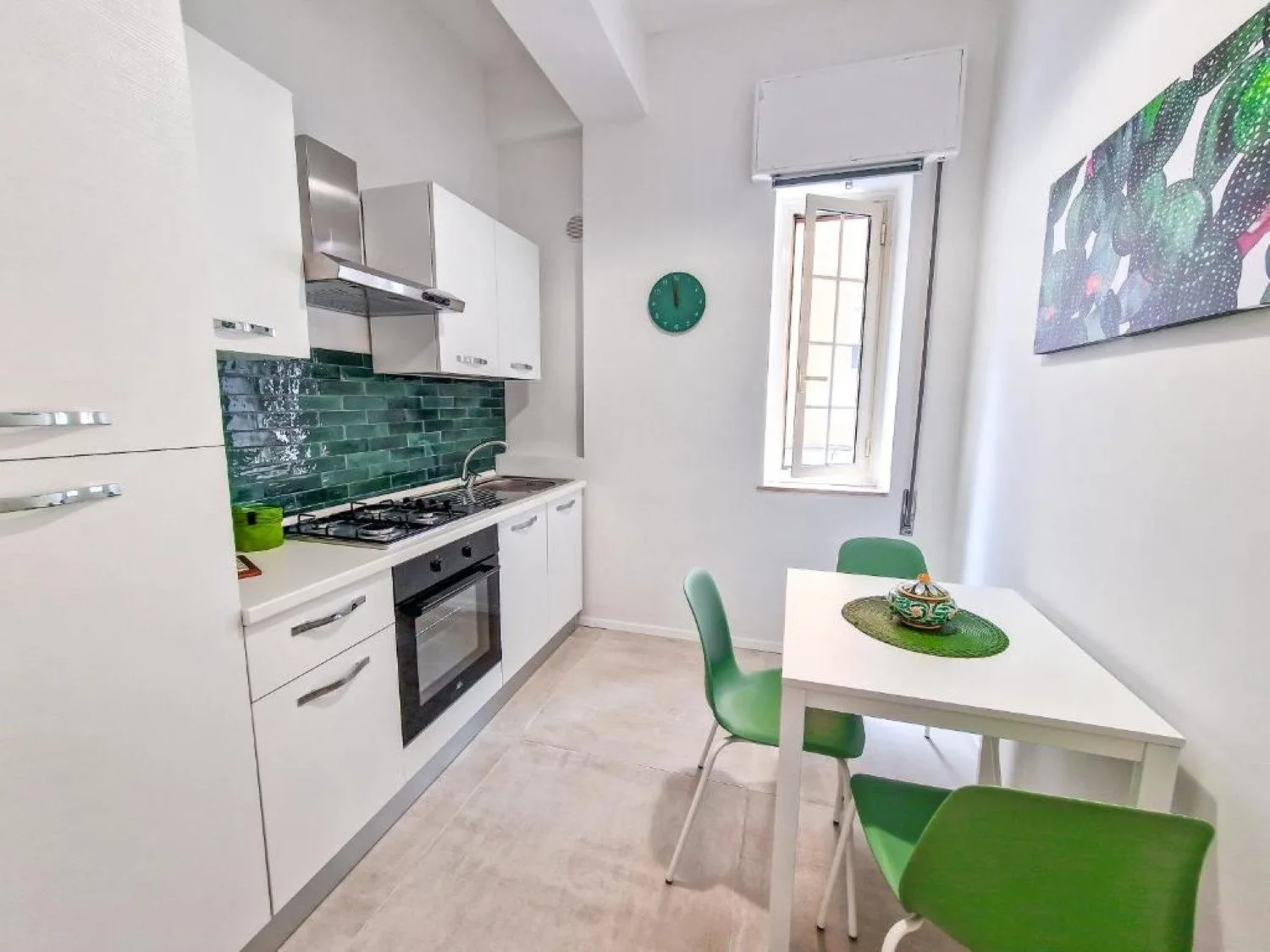 Una cocina luminosa con armarios blancos, un salpicadero verde y una pequeña mesa de comedor.