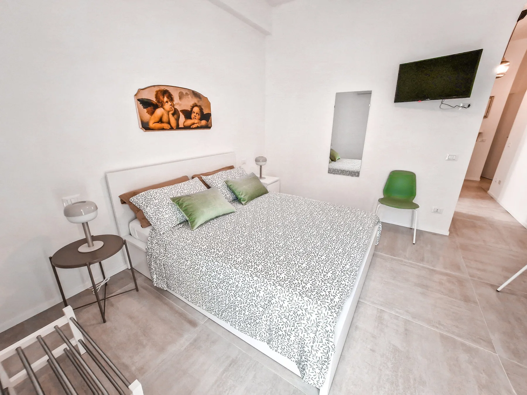 Un dormitorio con una cama doble, ropa de cama estampada y un televisor en la pared.