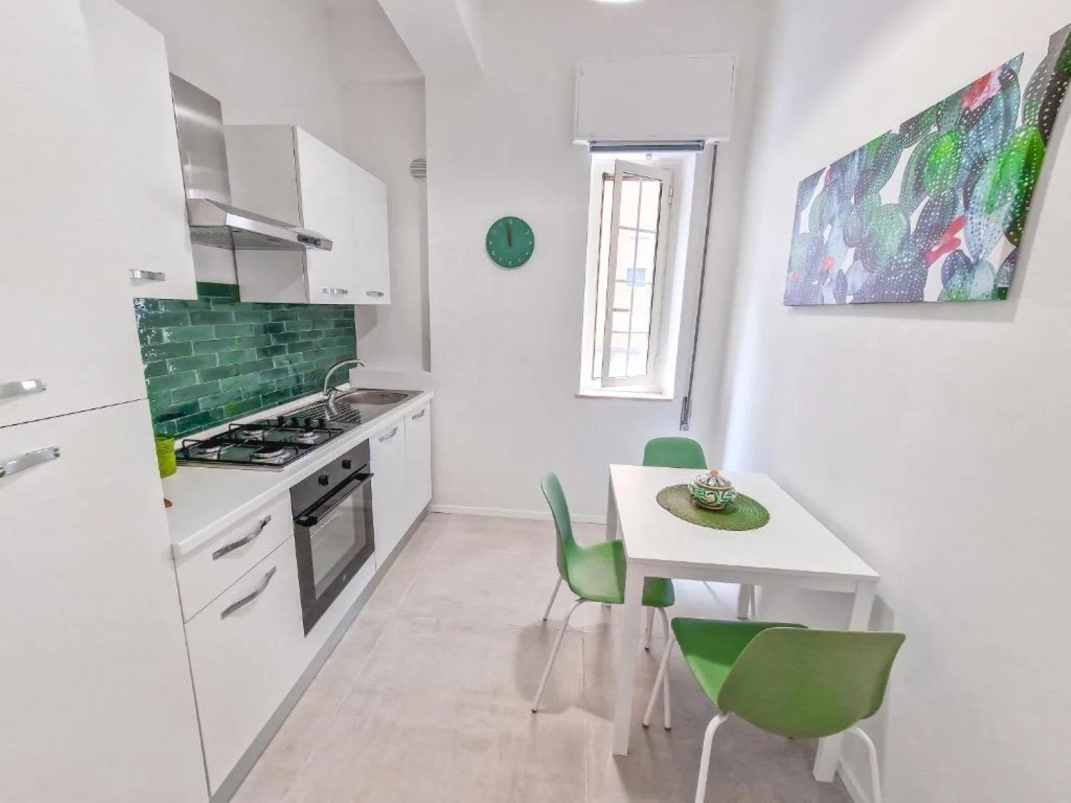 Una cocina luminosa con gabinetes blancos, detalles verdes y una mesa pequeña.
