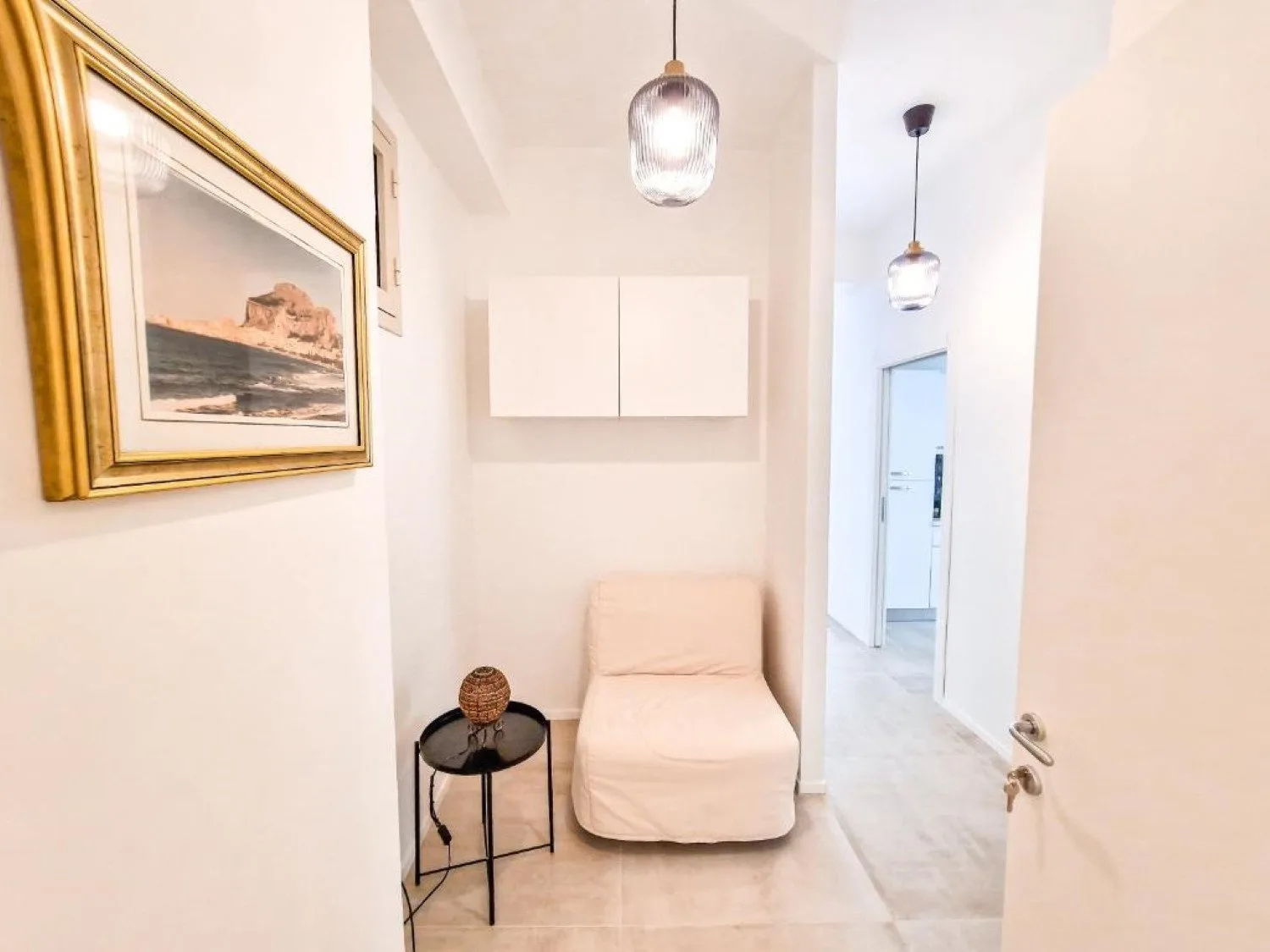Un pasillo luminoso con un asiento acolchado, un cuadro y lámparas colgantes.