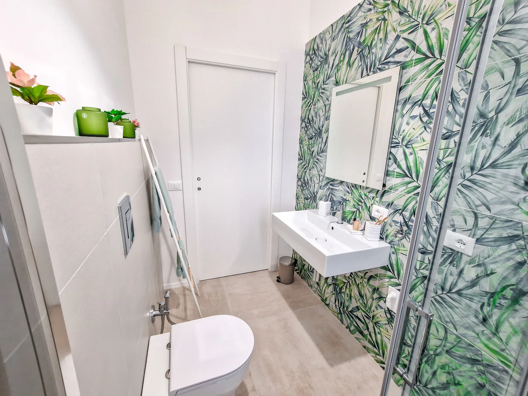 Un baño luminoso con lavabo mural y paredes con estampado de hojas.