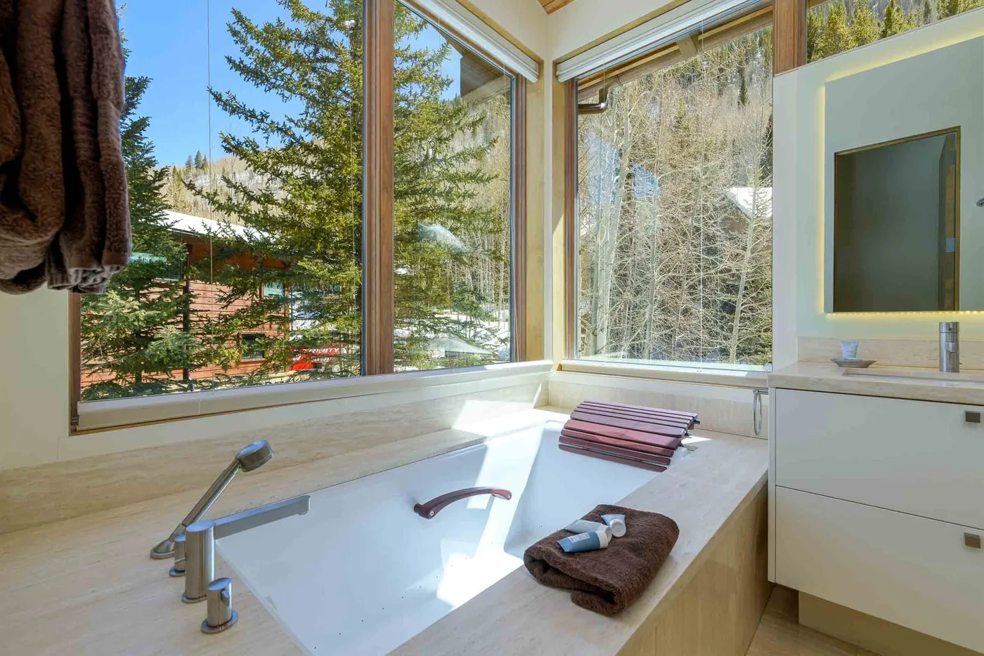 Un baño con una bañera amplia junto a grandes ventanas con vistas a los árboles.