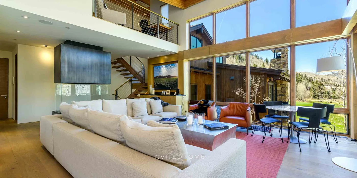 Una sala luminosa con asientos, comedor y grandes ventanas con vistas al exterior.
