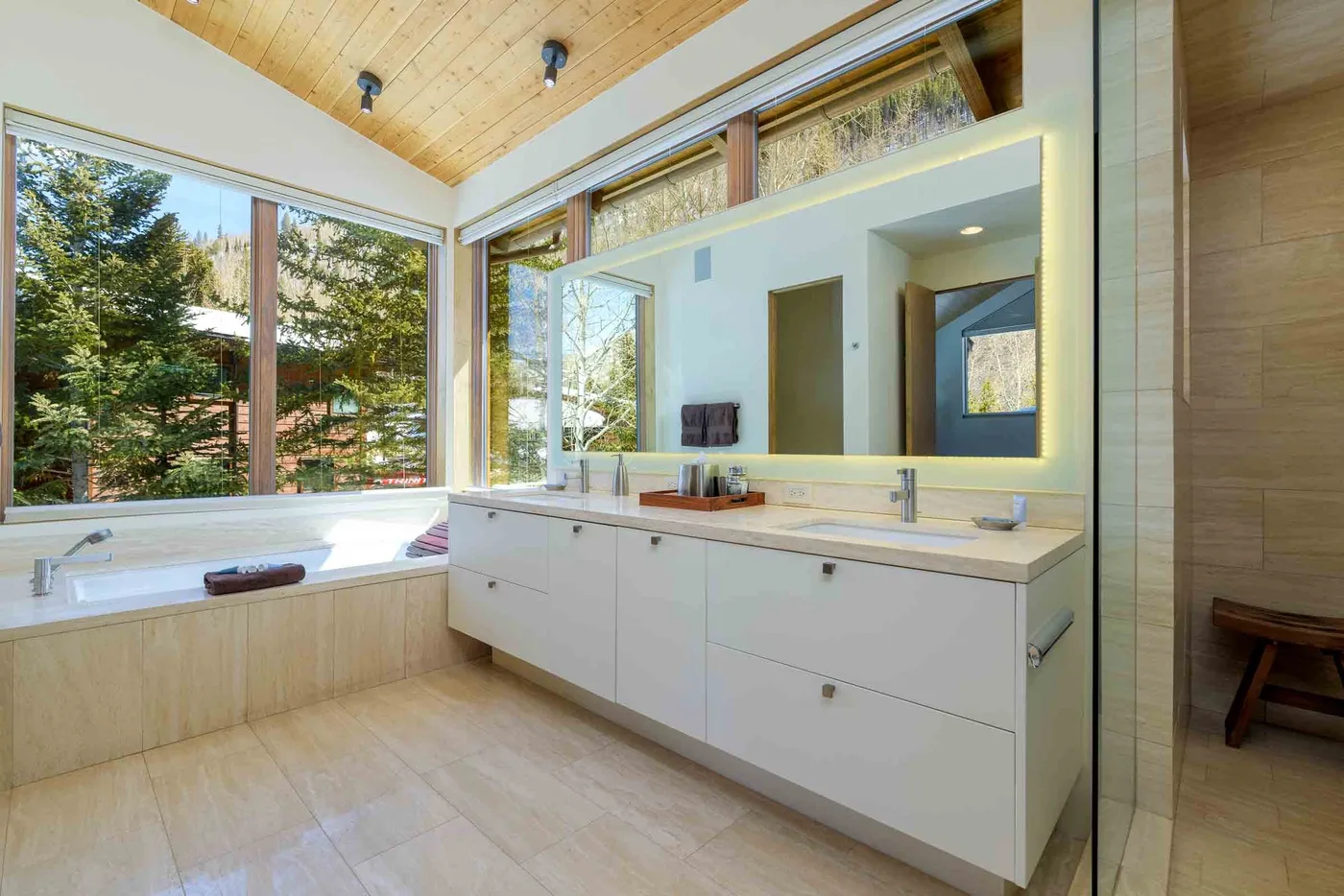 Un baño luminoso tiene una bañera bajo grandes ventanas y un tocador largo.