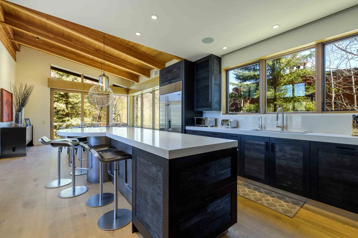 Una cocina moderna con isla central, gabinetes oscuros y ventanas grandes.
