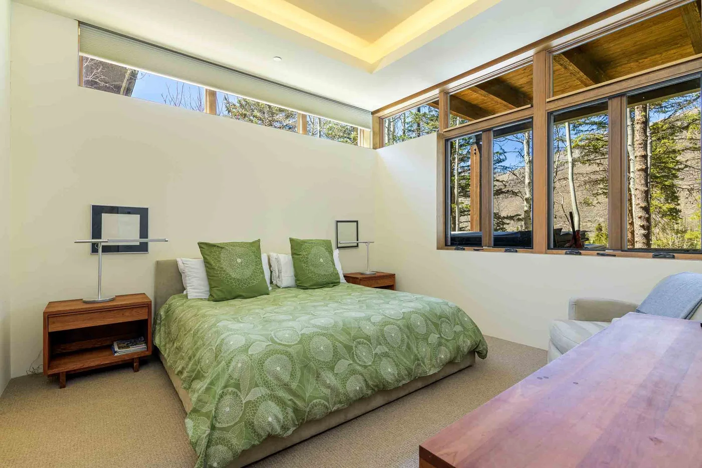 Un dormitorio con una colcha verde y grandes ventanas con vistas a los árboles.