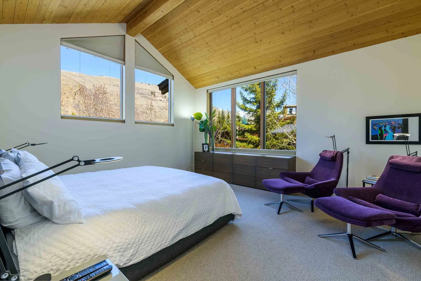 Dormitorio con una cama grande, asientos morados y amplias ventanas.