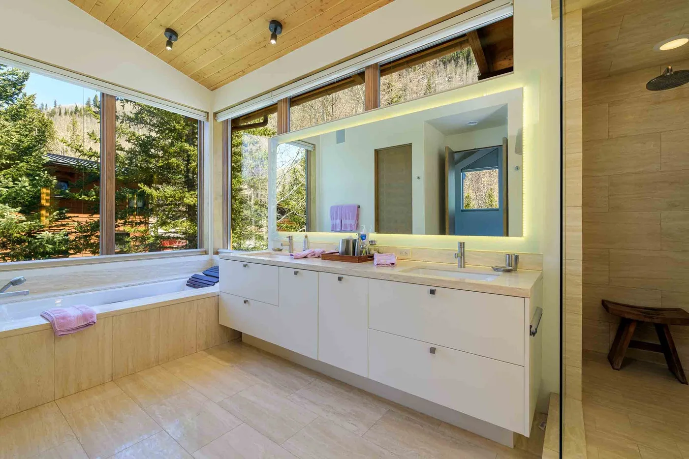 Un baño luminoso con un tocador largo, espejo iluminado y grandes ventanas.