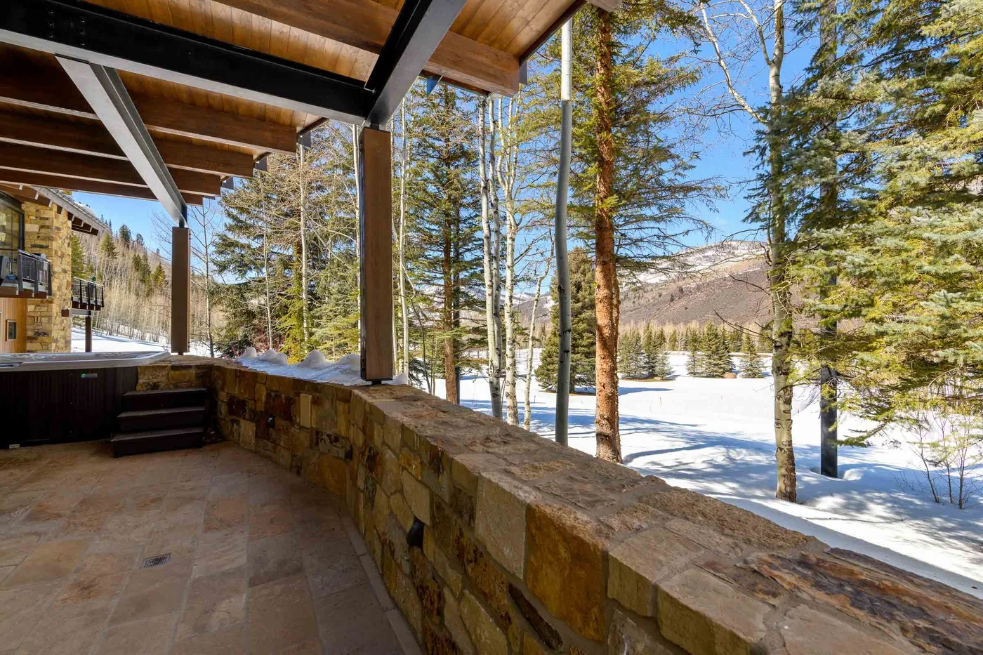 Un patio cubierto da a un paisaje nevado con árboles y montañas a lo lejos.