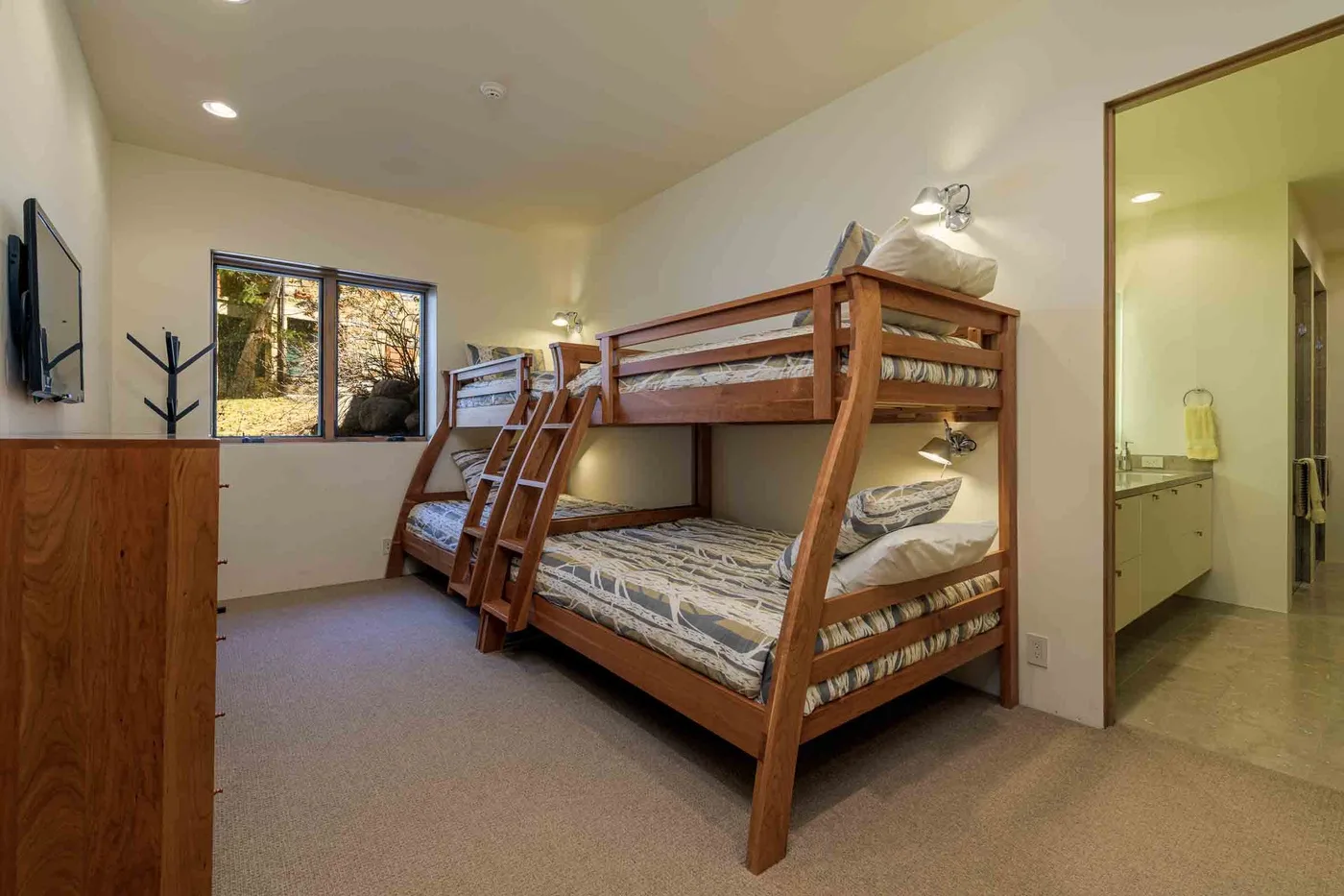 Dormitorio con literas de madera, una ventana y una puerta abierta hacia un baño.