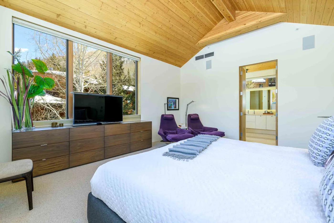 Un dormitorio con una cama grande, ventanales amplios y un techo de madera.