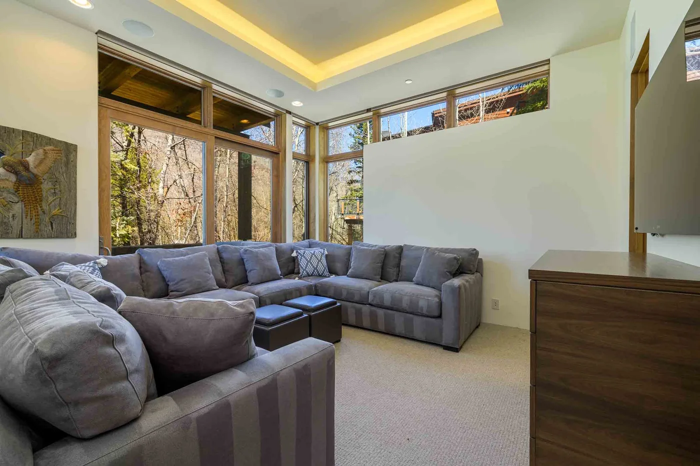 Una sala luminosa con asientos grises, grandes ventanas y una mesa de centro baja.