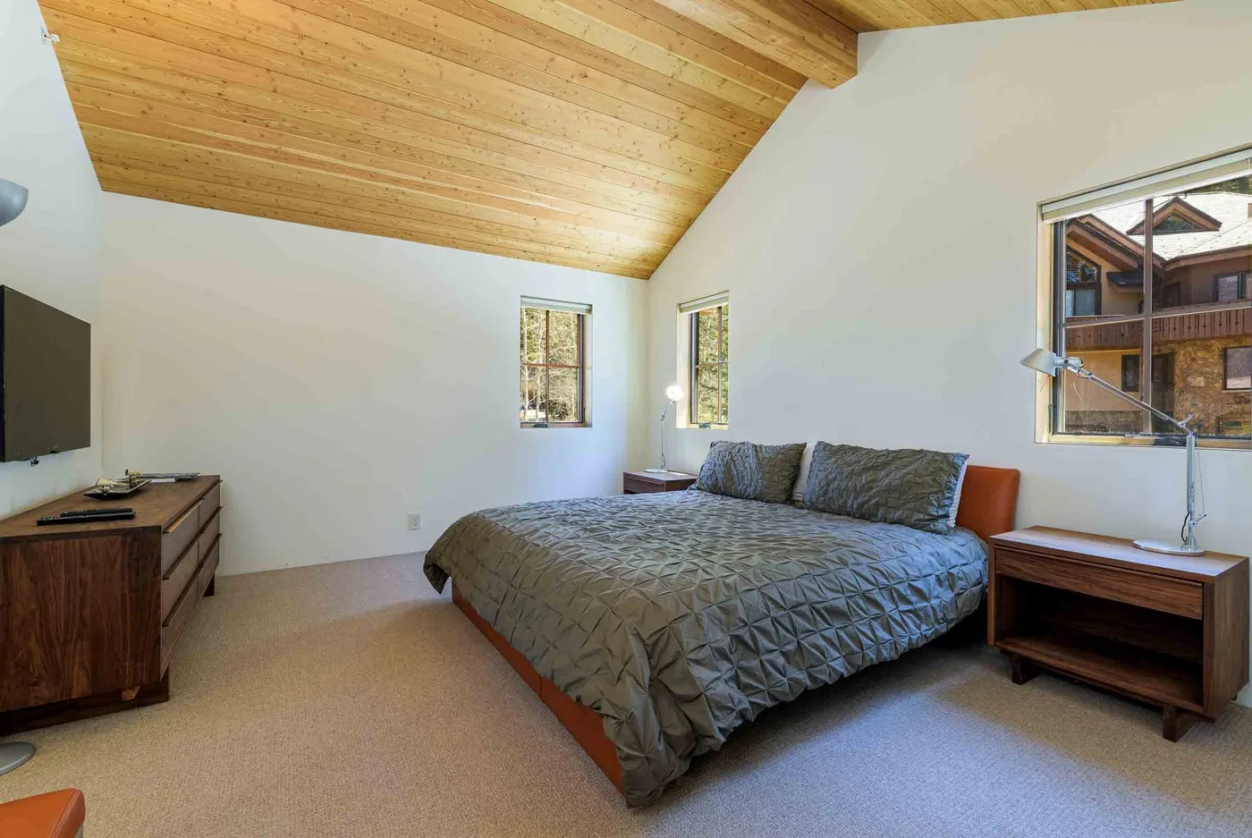 Un dormitorio con una cama doble, mesitas de noche y un techo inclinado de madera.