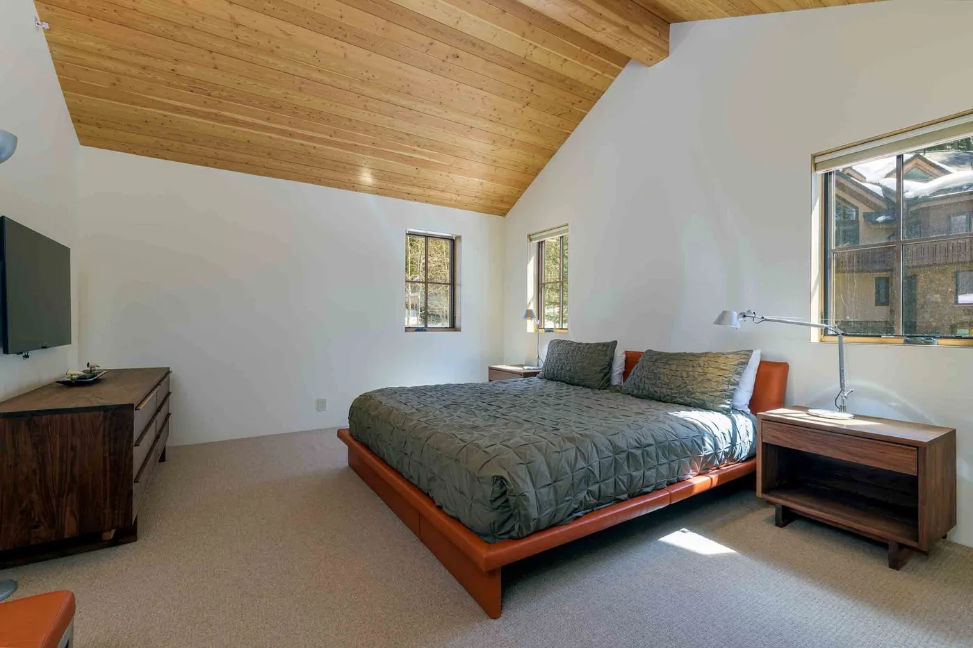 Dormitorio con una cama bajo un techo inclinado de madera y ventanas.