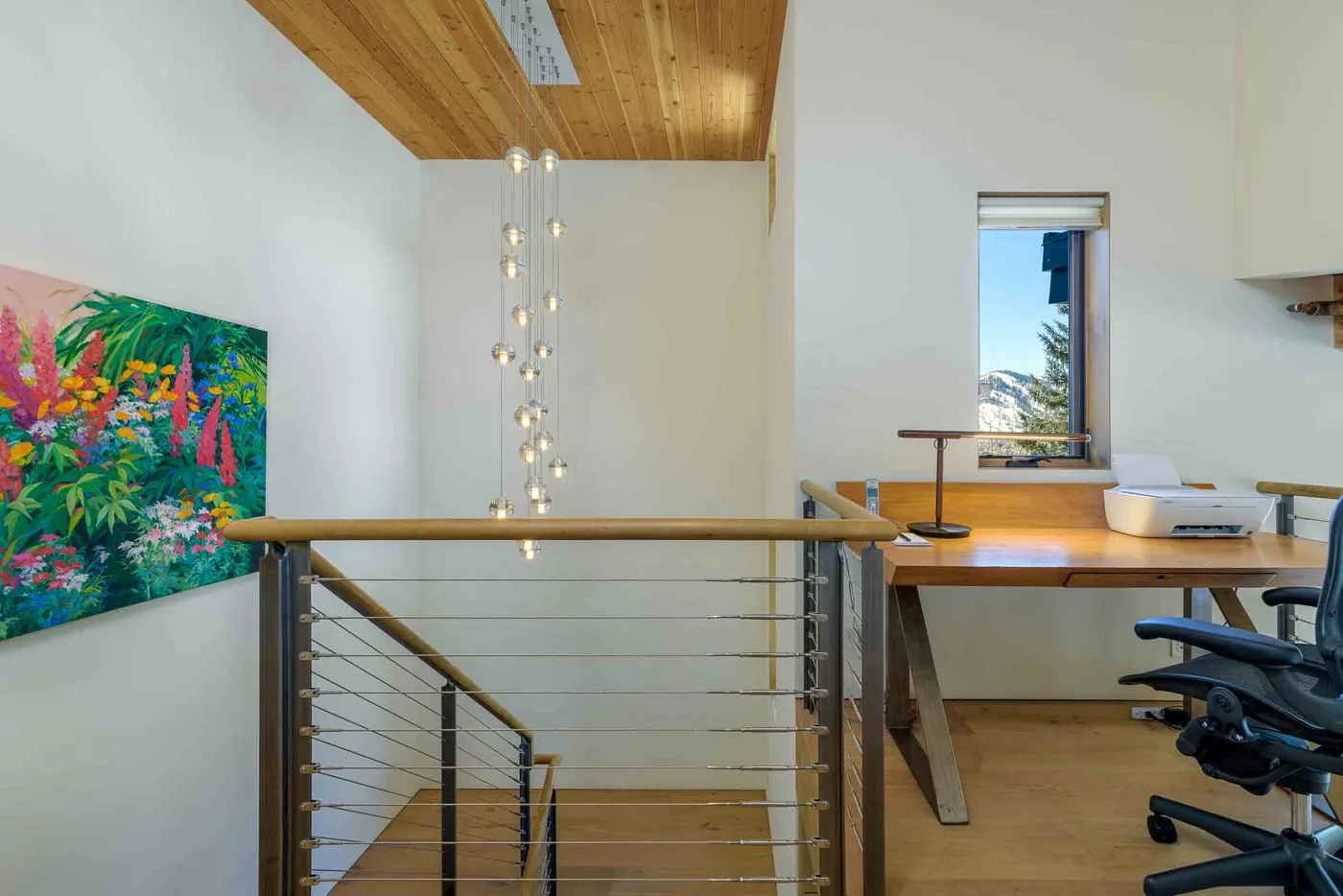 Un espacio de trabajo luminoso tipo loft, con escritorio junto a una barandilla y arte colorido en la pared.