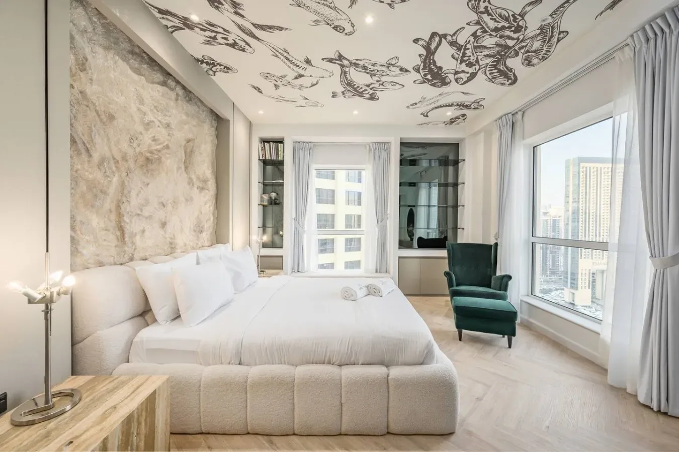 Un dormitorio luminoso con una cama grande, un sillón y amplias ventanas.