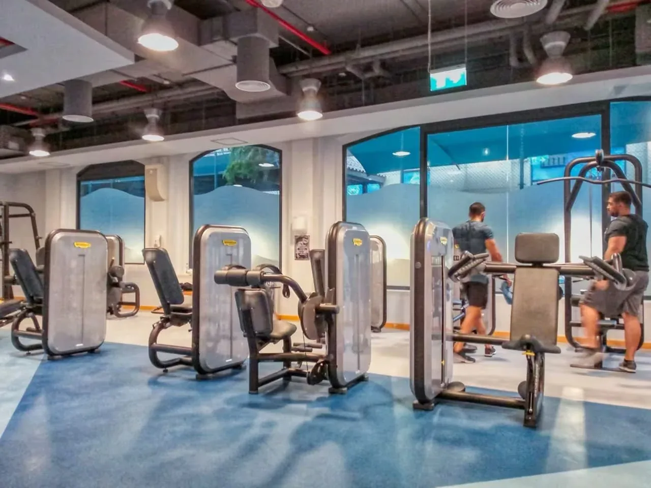 Un gimnasio con máquinas de ejercicio, pesas y personas entrenando.
