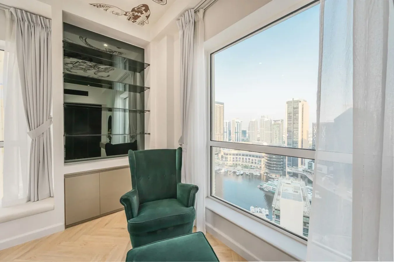 Una luminosa zona de estar con asientos verdes junto a una gran ventana con vistas a la ciudad.