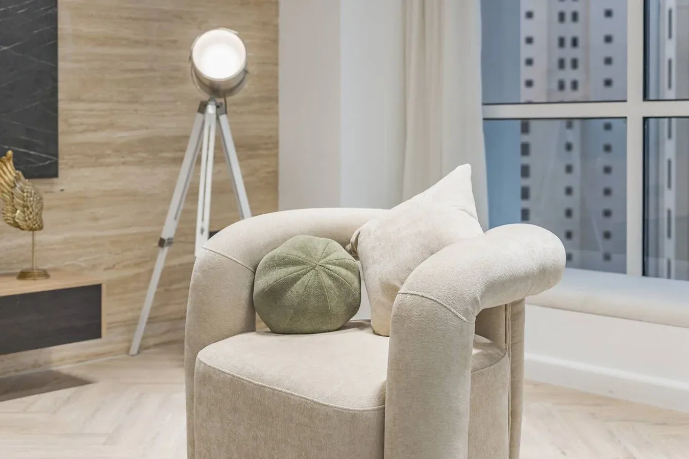 Un sillón claro con cojines está junto a una lámpara de pie con trípode en una sala de estar.