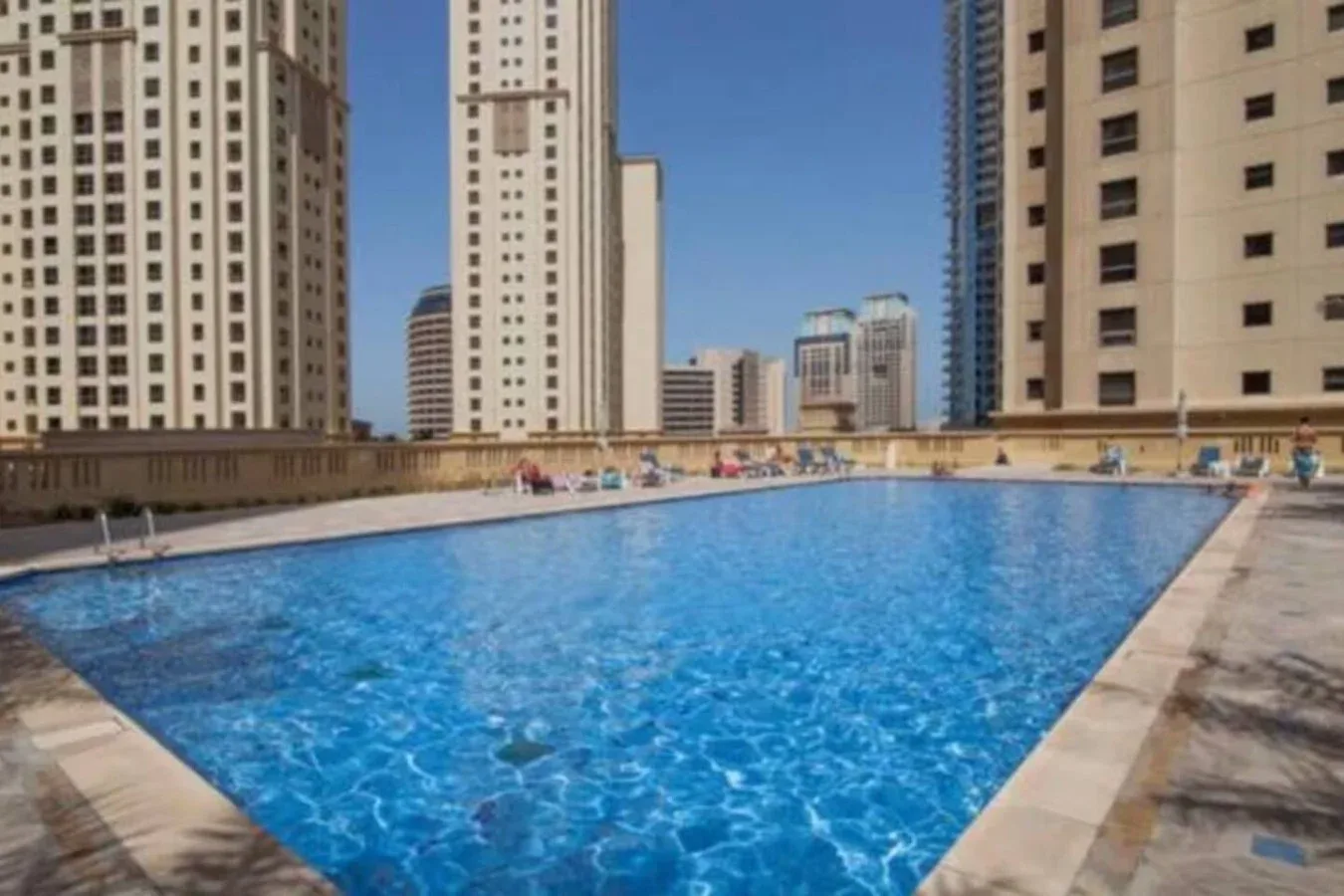 Una piscina está rodeada de edificios altos bajo un cielo azul despejado.