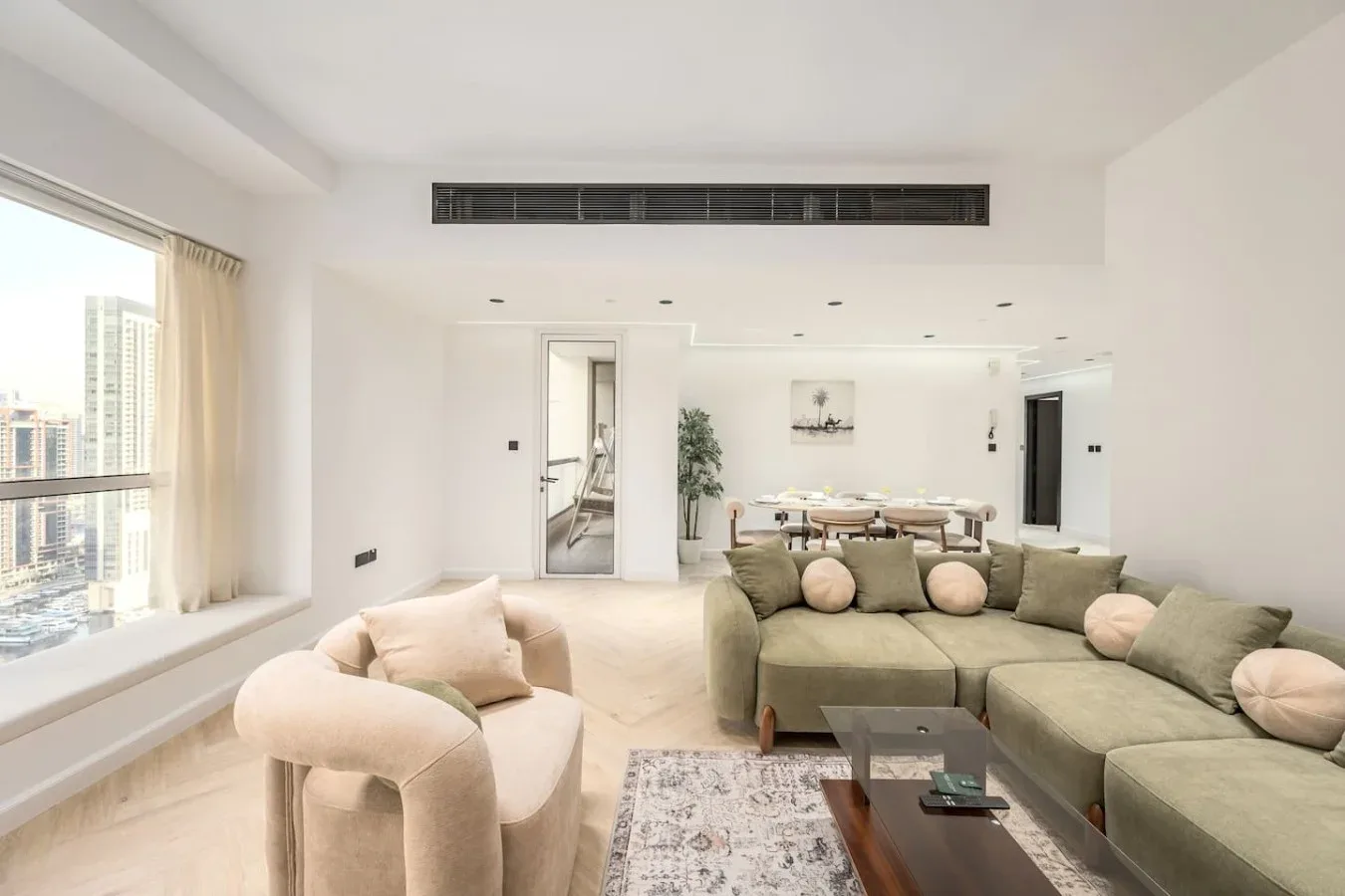 Una sala luminosa con una zona de asientos seccionales y un comedor al fondo.