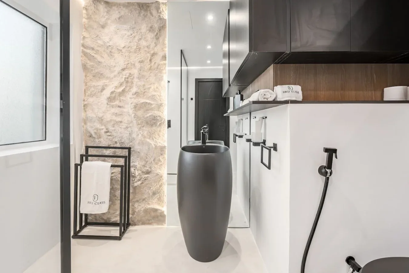 Un baño moderno con un lavabo exento, accesorios de pared y una pared decorativa de piedra.