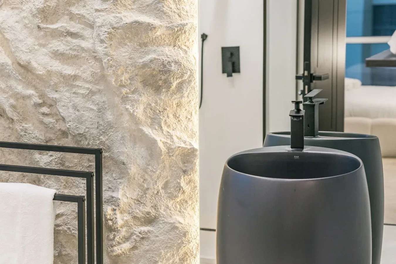 Un lavabo de baño con cuencos oscuros junto a una pared de piedra texturizada.