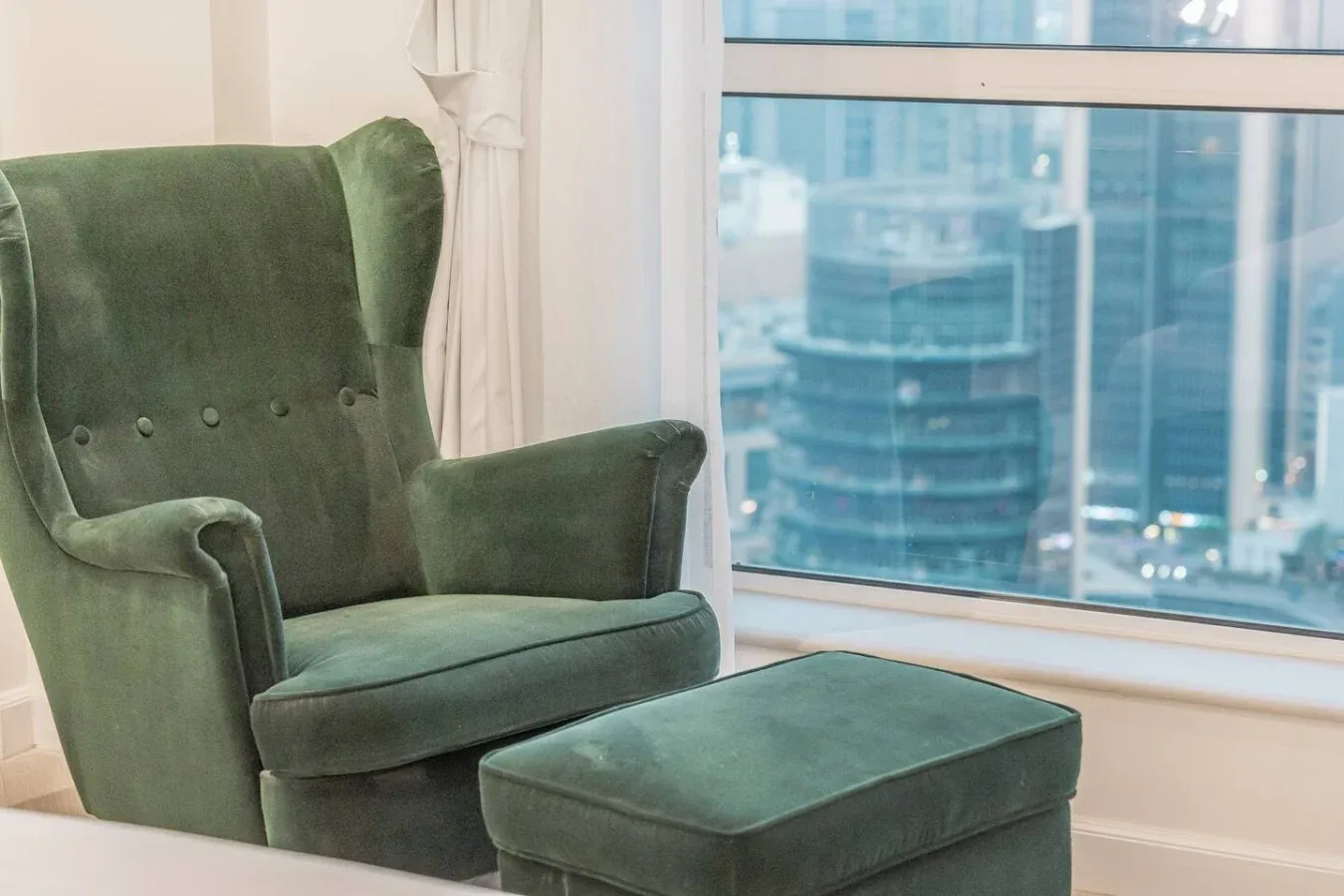 Una zona de estar con un sillón verde y un reposapiés a juego junto a una ventana grande.