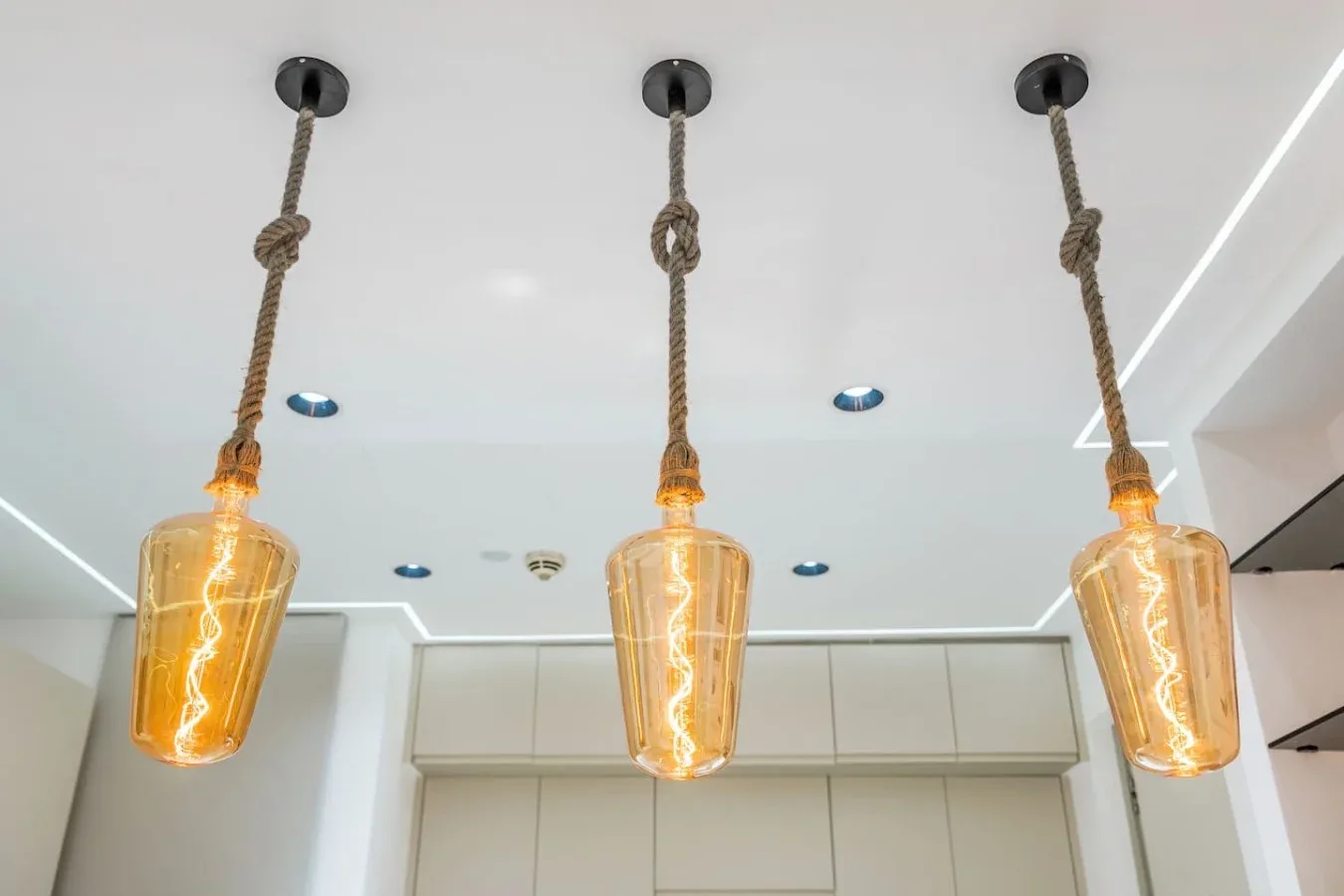 Tres lámparas colgantes ámbar cuelgan de cuerdas en un interior luminoso.