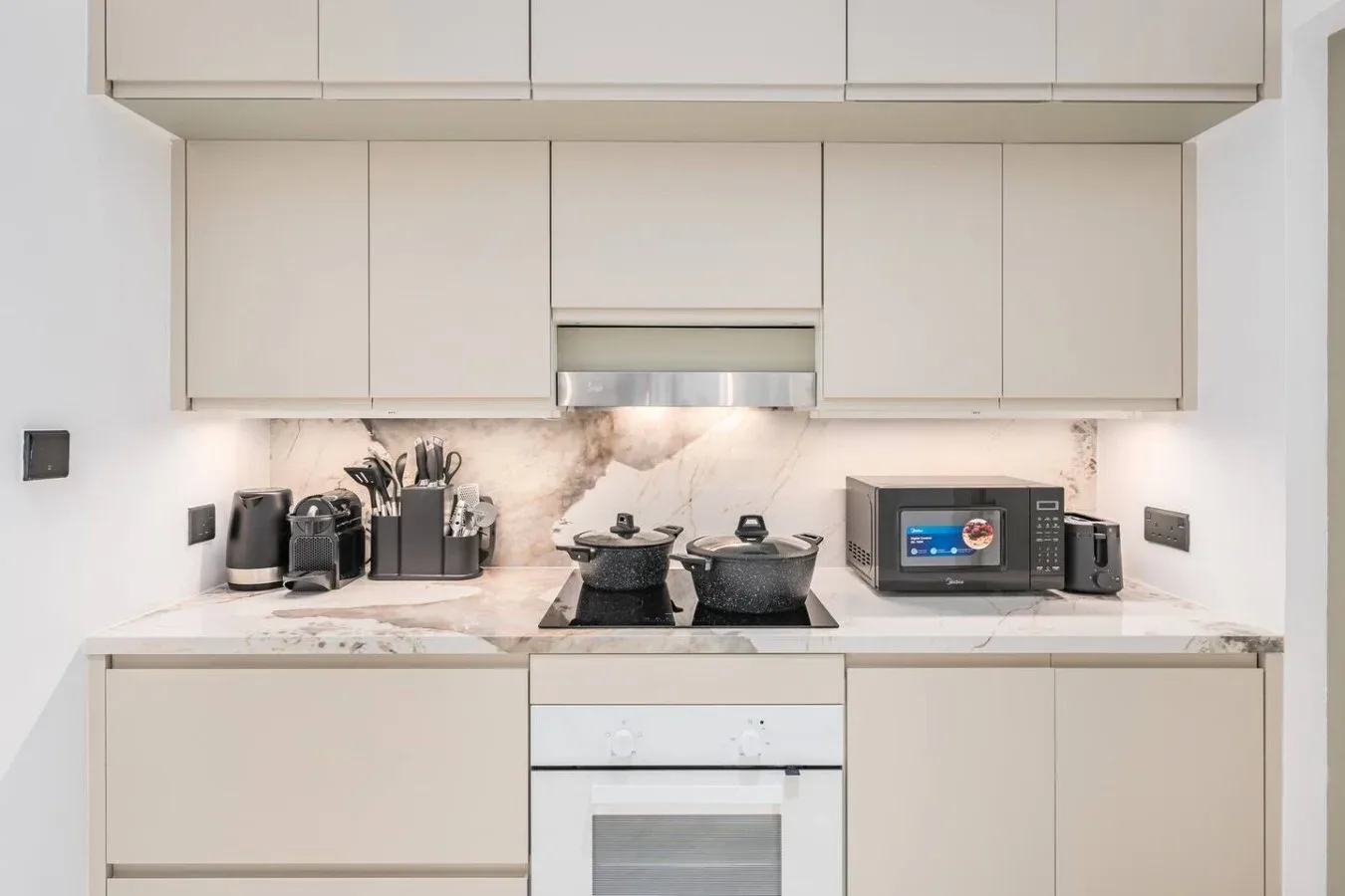 Una cocina moderna con gabinetes claros, una placa de cocina y electrodomésticos sobre la encimera.