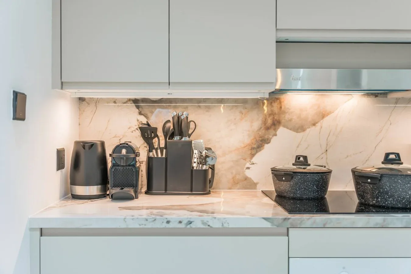 Una encimera de cocina moderna con pequeños electrodomésticos y utensilios bajo armarios superiores.