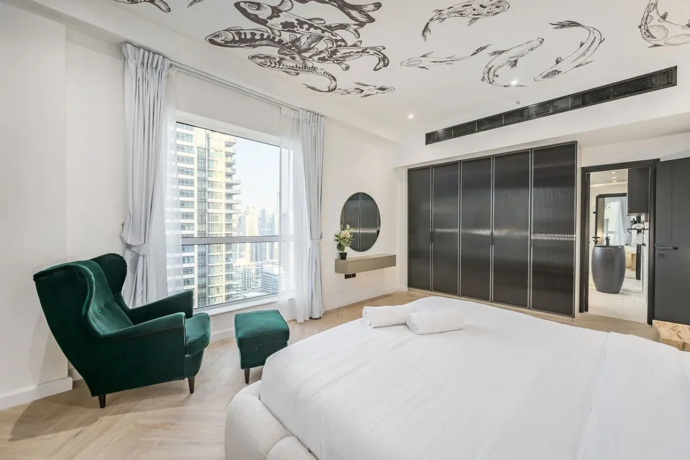 Un dormitorio luminoso con una cama grande, asientos verdes y una ventana amplia.