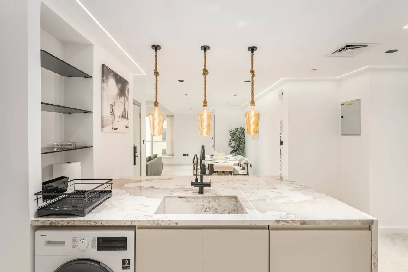 Una cocina luminosa con isla de mármol, fregadero y lámparas colgantes.