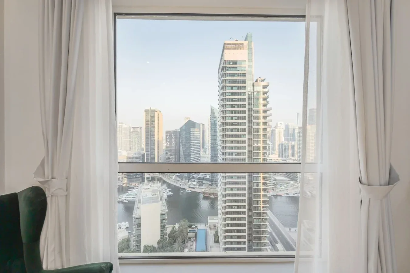 Un horizonte urbano se ve a través de una gran ventana enmarcada por cortinas blancas.