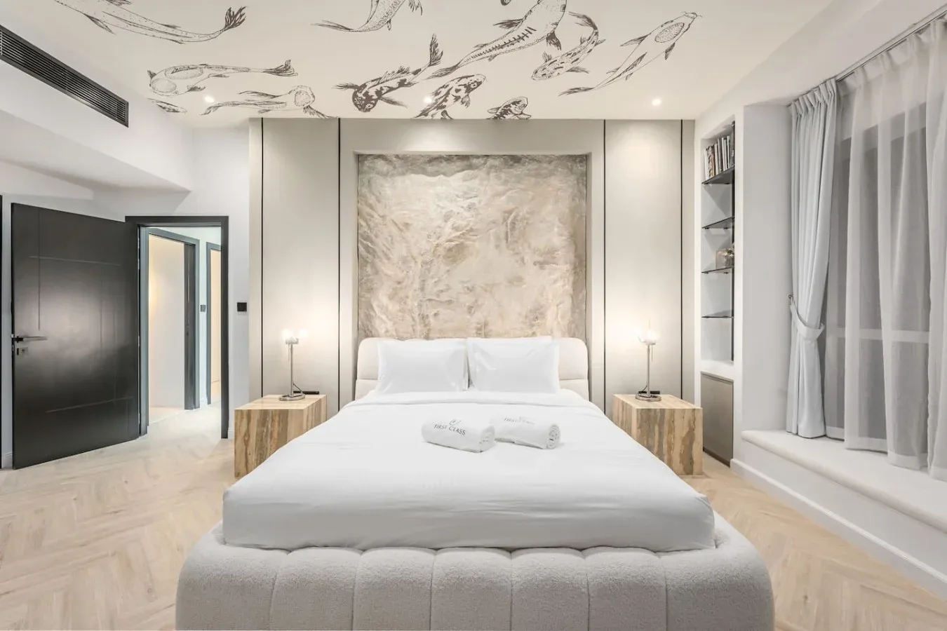 Un dormitorio luminoso con una cama grande, un panel de pared estampado y cortinas largas.