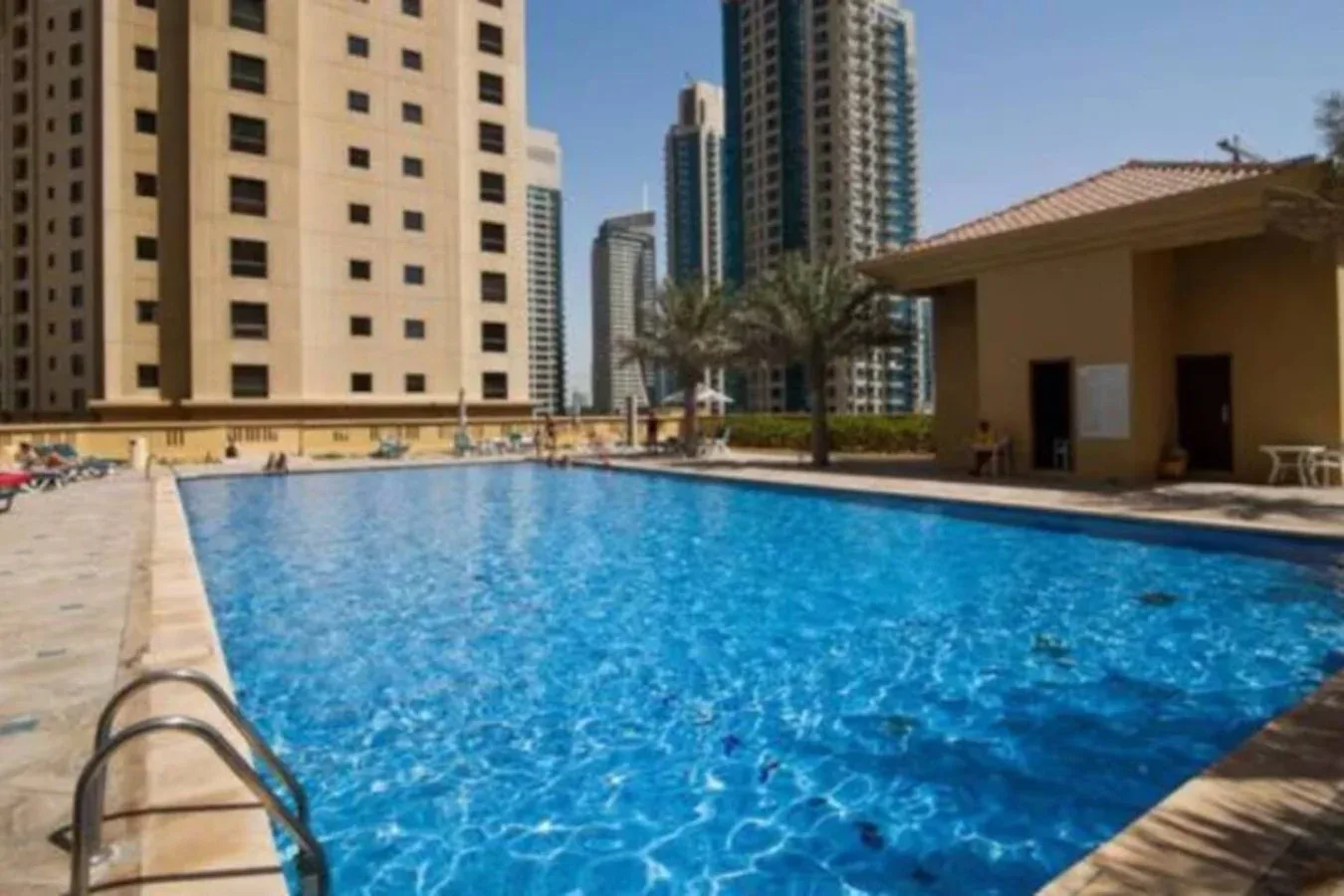 Una piscina al aire libre está junto a un edificio pequeño y torres residenciales.