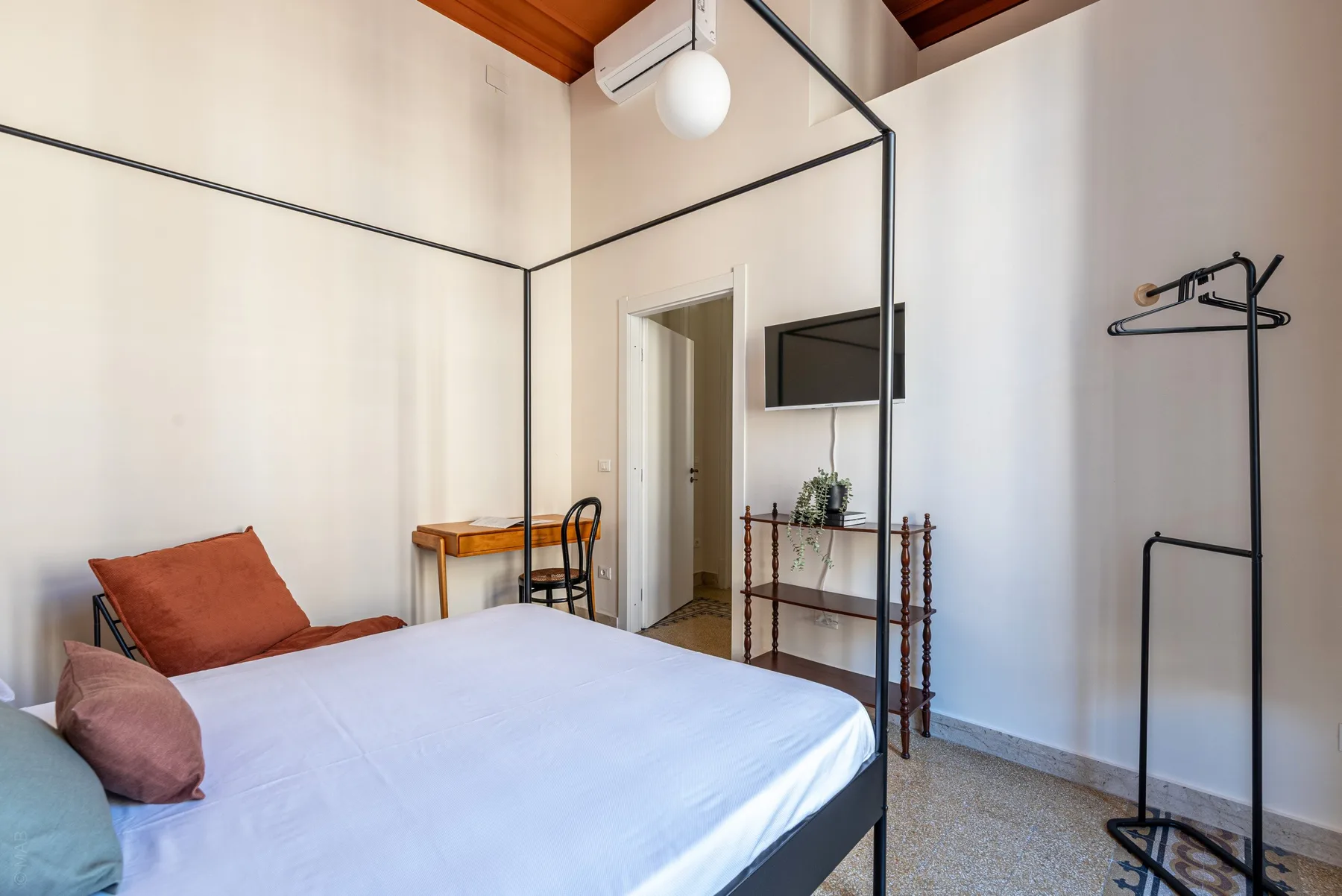 A bedroom with a bed, a small desk, and a wall-mounted television.