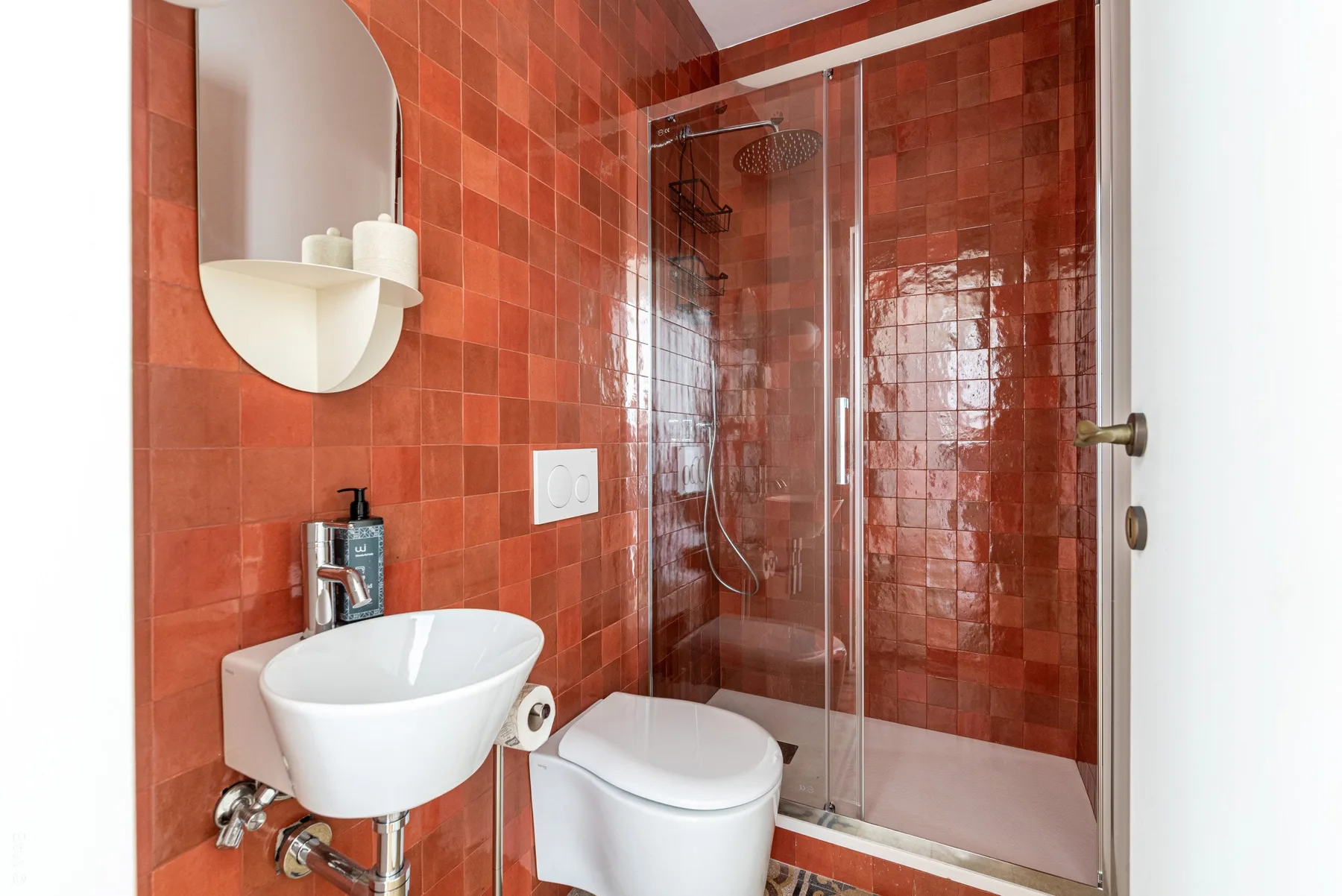 A bathroom with a wall-mounted sink, toilet, and glass shower.